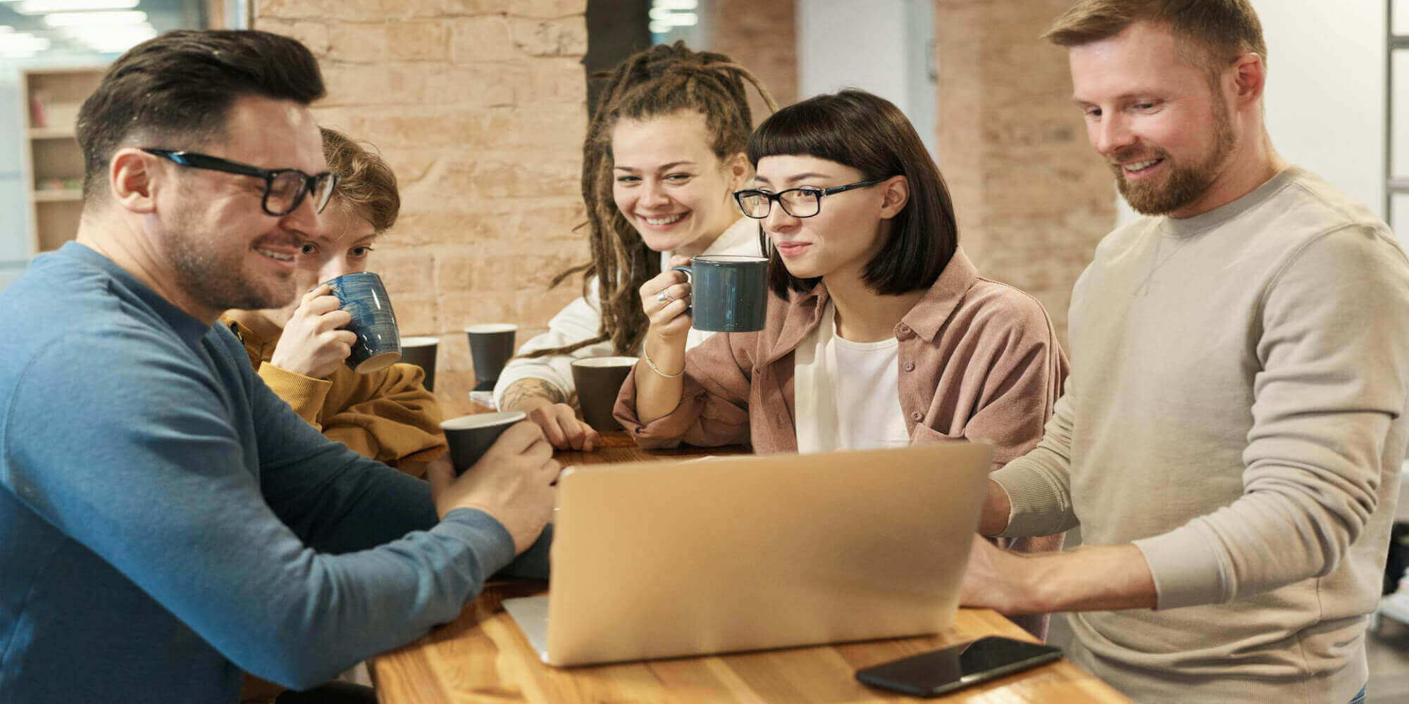 Gruppe von Menschen, Männer und Frauen, am modernen Arbeitsplatz mit Laptop, Tablet und Smartphone. Sie stehen für körperliche Gesundheit und trinken Kaffee und Tee.