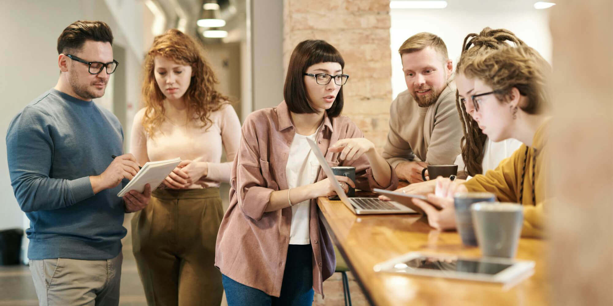 Eine Gruppe von Personen bei einem internen Meeting mit Laptop, Tablet, Smartphone und Notizbuch in modernem Büro.