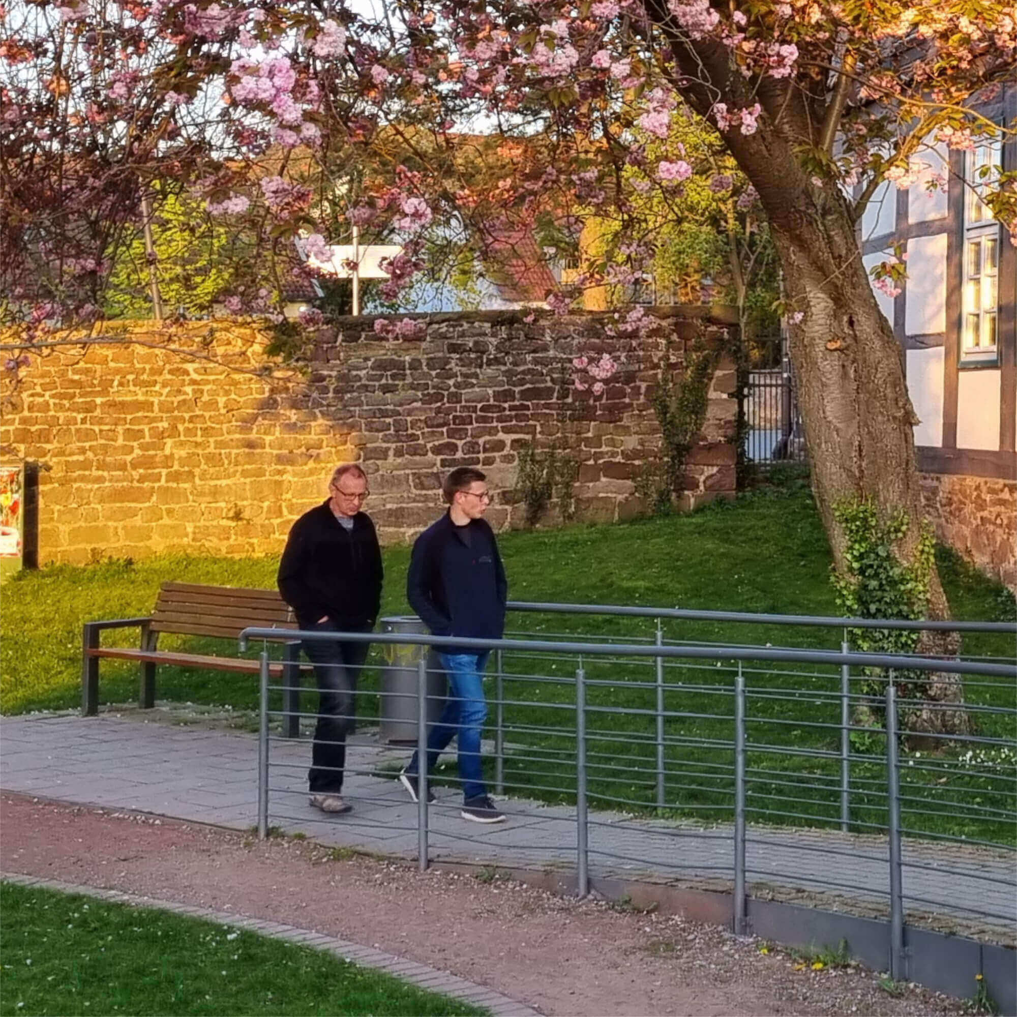 Vater - Martin Matheus und Sohn - Aron Matheus spazieren entspannt durch einen Stadtpark und unterhalten sich.