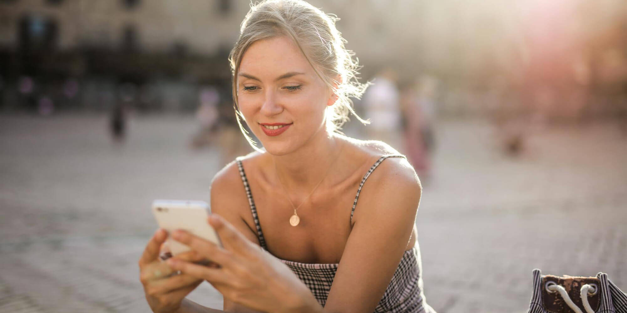 Lächelnde und hübsche Frau benutzt Smartphone auf belebtem Platz.